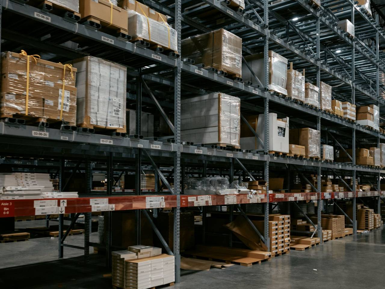 Interior de una bodega con estanterías altas, pallets y cajas