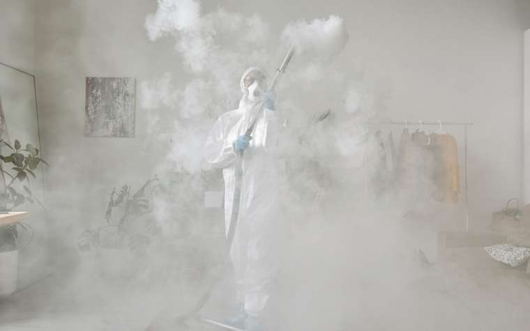 Persona con traje de protección sanitizando un ambiente con nebulización en frío